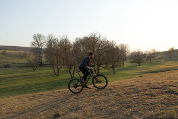 Obraz premium Cyclist in shorts and jersey on a modern carbon hardtail bike with an air suspension fork standing on a cliff against the background of fresh green spring forest