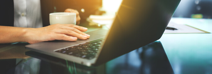 Businesswoman using and touching on laptop touchpad while drinking coffee in office
