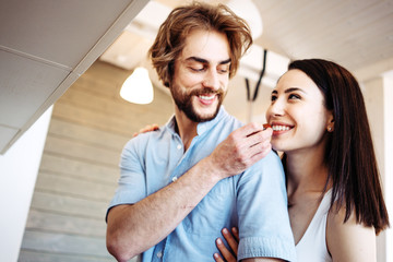 Romantic couple spending time together at the kitchen. Smiling man feeding pretty woman