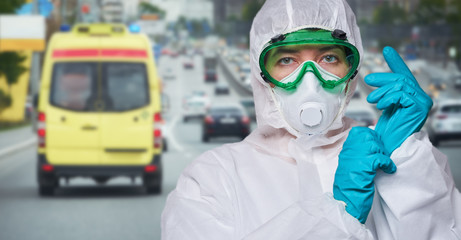 Doctor is wearing PPE - costume, gloves and surgical face mask against city background.