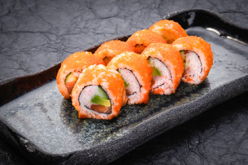 Sushi set served on dark background. Maki roll, Philadelphia maki with masago, salmon, cream cheese, avocado and prawn. Assorted sushi. Japanese food. Restaurant menu. Side view, close up