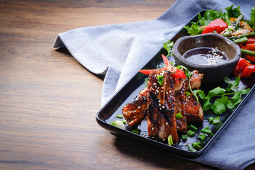 Grilled and smoked ribs with salad and bbq sauce on a plate on wooden table background. Meat dish....