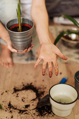 A young woman shows her hands after transplanting flowers Concept of home garden. Spring time. Stylish interior with a lot of plants. Taking care of home plants.