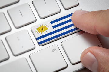 Online International Business concept: Computer key with the Uruguay on it. Male hand pressing computer key with Uruguay flag.