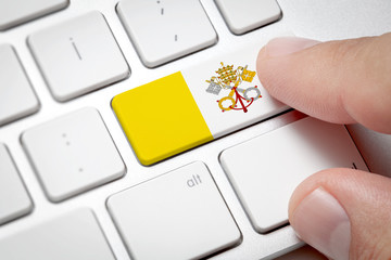 Online International Business concept: Computer key with the Vatican on it. Male hand pressing computer key with Vatican flag.