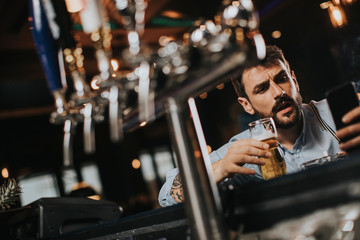 Man drinking beer, smoking cigarette and using mobile phone at pub
