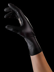 Hand in black gloves holding something with two fingers isolated on black