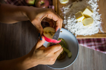 Fototapeta na wymiar Girl peels apples by hands into a bowl to prepare apple pie
