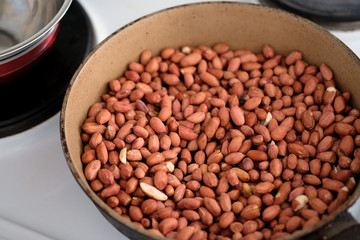The peanuts in the peel are roasted in a pan. Nuts are fried on a stove in a pan top view.