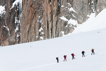 Teamwork in the mountain and business concept. Group of ski mountaineers ascending in the snow with big rock walls in background. Argentiere glacier, Chamonix, France, Europe, Alps.