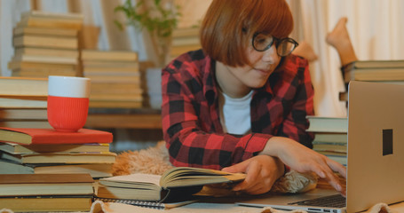 Young woman student studying at home with many books and laptop	
