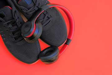 Black fabric sneakers and on-ear headphones on a red background. Men's sneakers with laces and headphones top view. The concept of a sports lifestyle, activities with your favorite music.