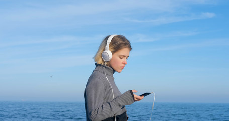 Young handsome female listen to music with headphones outdoor on the beach against sunny blue sky	