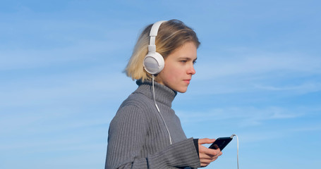 Young handsome female listen to music with headphones outdoor on the beach against sunny blue sky	 - 352144549