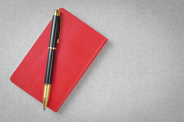 Black and gold fountain pen placed on red notebook on gray cement texture background and space.
