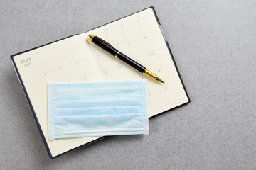 Black and gold fountain pen placed on blank planner book with medical protective mask on gray cement texture background. Work and health concept.