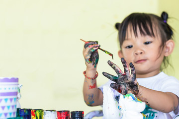 Selective focus at dirty hand of Asian child baby girl drawing and painting colours on the paper in the room. Study​ from​ home, social​ Distance, Kid and education concept. 2-3 years old of child.