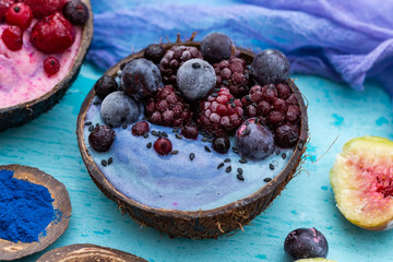 Coconut bowl of frozen raspberries and blackberries on a cyan worn out table top with blue cream. Smoothie bowl with frozen summer fruit.