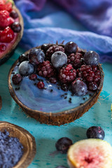 Coconut bowl of frozen raspberries and blackberries on a cyan worn out table top with blue cream. Smoothie bowl with frozen summer fruit.