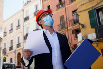 Ingegnere con casco arancione e mascherina Chirurgica lavora in un cantiere in città 