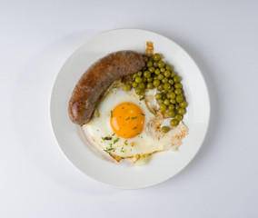 Homemade delicious sausage, fried eggs and green peas on a plate. Top view