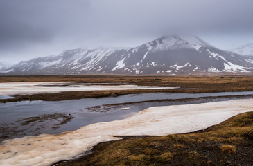 Meadow with snow and frozen lake and snowcapped mountains. Iceland