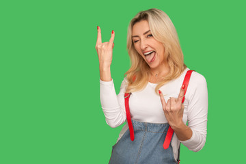 That's crazy! Portrait of delighted adult woman in stylish denim overalls showing rock and roll...