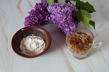 Natural home skin care. Ingredients of a face mask. Decoction of lilac flowers (Syringa vulgaris) and potato starch close-up on a marble background. Selective focus.