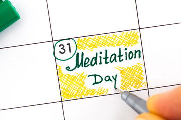 Woman fingers with pen writing reminder Meditation Day in calendar.