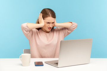 Don't want to hear you. Angry woman employee covering ears and looking irritably at laptop screen, annoyed by unpleasant communication on video call. indoor studio shot isolated on blue background