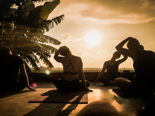 silhouette of a group of people doing yoga at sunset in the tropics with palm tree and rice fields...