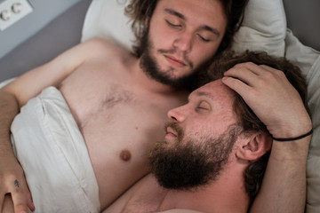 Close up of a gay couple hugging in bed.