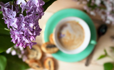 The flower arrangement is made of lilac flowers on a light wooden background with a Cup of coffee.