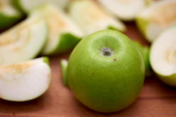 Green apples sliced far away lie on a wooden tabletop.