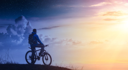 Fototapeta na wymiar Cyclist on a mountain top between day and night