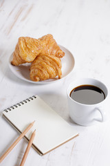 cup of hot coffee with croissant on white wooden background.  Working at home concept.