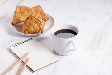cup of hot coffee with croissant on white wooden background.  Working at home concept.