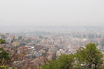 Fototapeta na wymiar Cityscape of Kathmandu city in Nepal. Smog covers the sky. Most of buildings made from red bricks. Residential architecture theme. View from Swayambhunath Stupa. Selective focus.