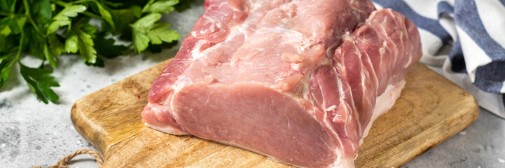 Raw pork carbonade on a wooden plate on the light gray kitchen table. Raw pork meat, tenderloin. Banner	
