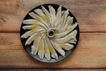 Portion of anchovies in vinegar with a splash of olive oil on black plate top view