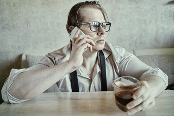 A man with a glass of whiskey in a shirt and tie is talking on a smartphone.