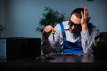 Young male technician repairing computer in workshop at night