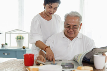 An Asian elderly couple reading a newspaper.