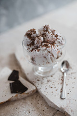 Vanilla ice cream sprinkled with chocolate chips and strawberry syrup in a transparent bowl on a light stone background