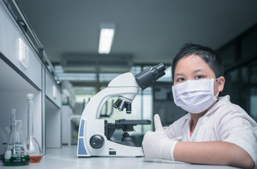 Fototapeta na wymiar cute asian scientist boy wear mask and working with microscope in laboratory,