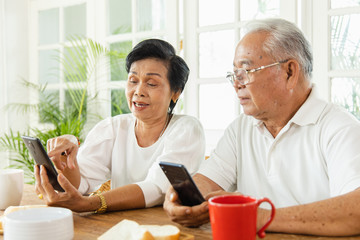 Portrait of an elderly Asian couple following the daily news by smartphone while eating breakfast. They enjoy and smiling faces. The activity of retirement age