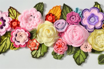 Multicolored crocheted flowers and leaves close up on a white background.