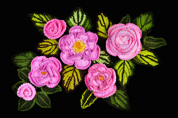 Handmade decoration made of freeform crocheted flowers and leaves isolated on black background.