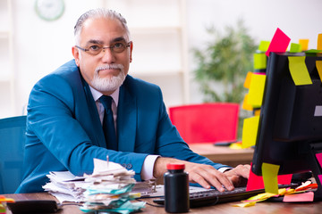Old employee working in the office in conflicting priorities