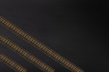 Pattern of gold colored paper clips on a black paper background. Paperclip.